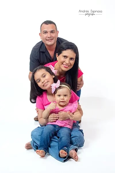 Familia feliz posando junta con dos niñas pequeñas, todos vestidos de rosa y sonriendo a la cámara.